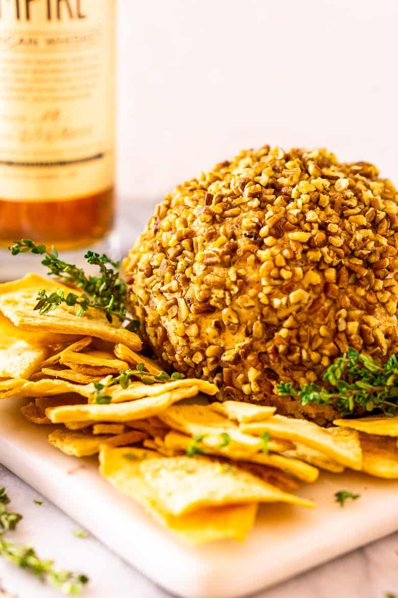 A bourbon bacon jam cheese ball with a bottle of bourbon in the background.