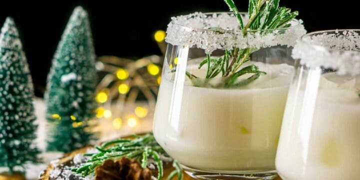 A Winter Wonderland Margarita on a wood board with candied rosemary and fake trees and lights in the background.