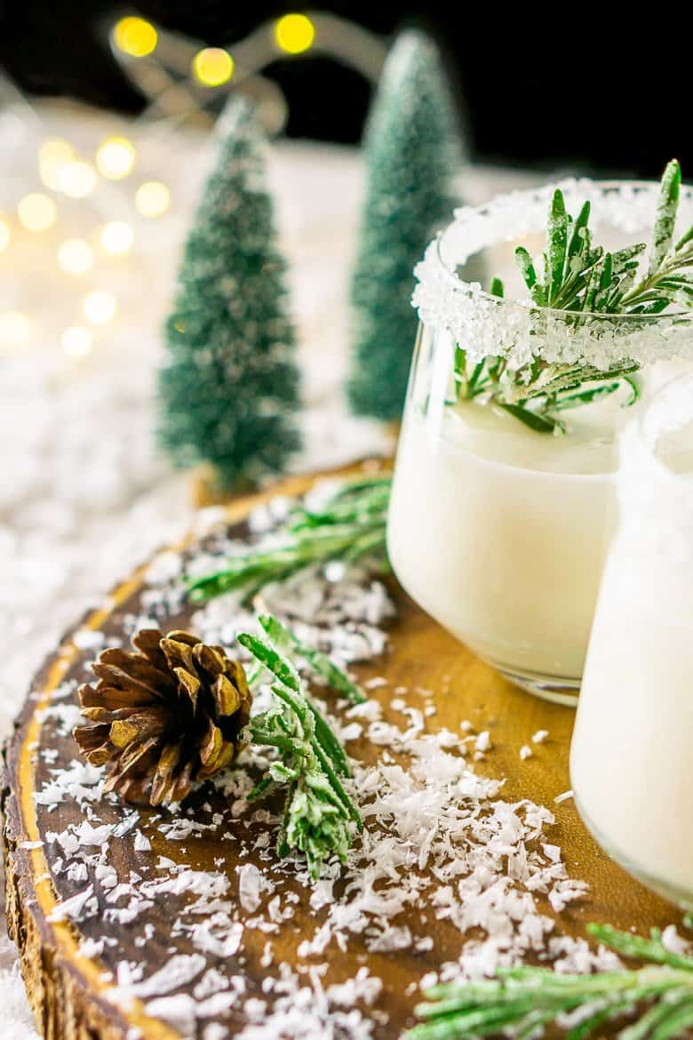 A winter margarita with a pine cone and candied rosemary surrounding it.