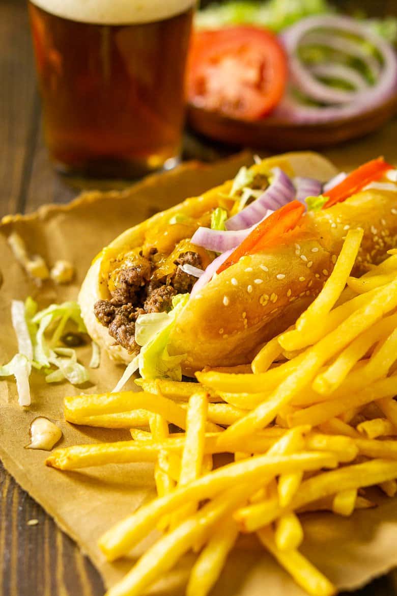 The cheeseburger sub with a beer and fries and special sauce on the brown paper.