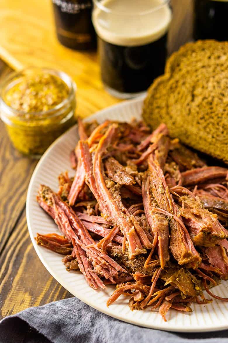 A plate of slow cooker corned beef with a wooden tray holding two Guinness pints.