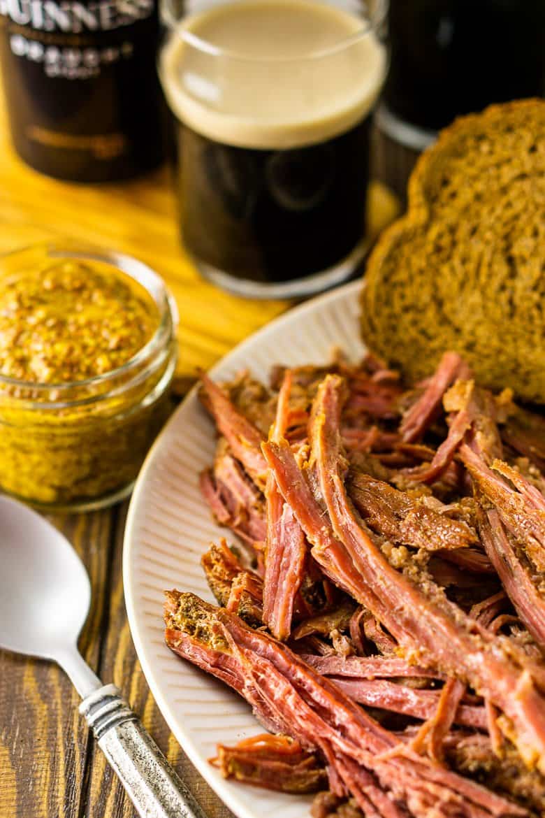 A close-up of the corned beef with mustard and a spoon on the side and rye bread in the background.