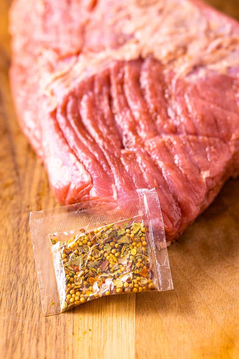 A slab of corned beef on a cutting board with the seasoning packet.