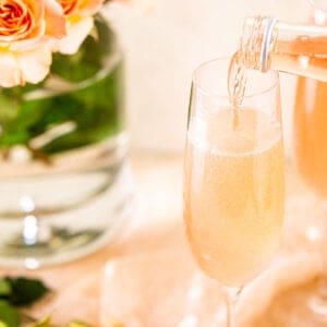 A bottle of wine filling the sparkling rose French 75 champagne glass with flowers behind it.