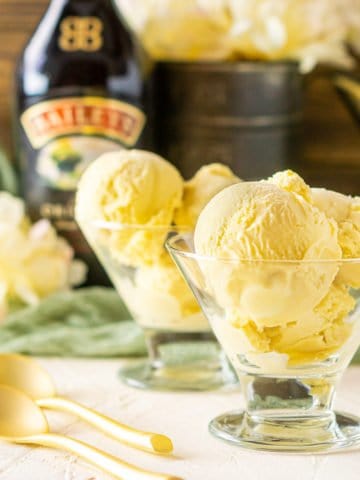 A glass cup holding a few scoops of Baileys ice cream with a bottle of Irish cream in the background.