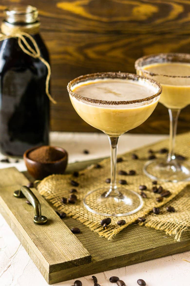 Two Baileys Irish coffee martinis on a wooden platter with coffee beans and a glass bottle of cold-brew coffee.