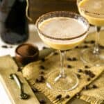 A Baileys Irish coffee martini in a coupe glass on burlap and a wooden platter.