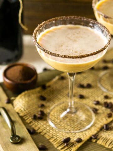 A Baileys Irish coffee martini in a coupe glass on burlap and a wooden platter.