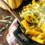 A cast-iron skillet filled with chorizo and pumpkin baked ziti with a wooden serving spoon.