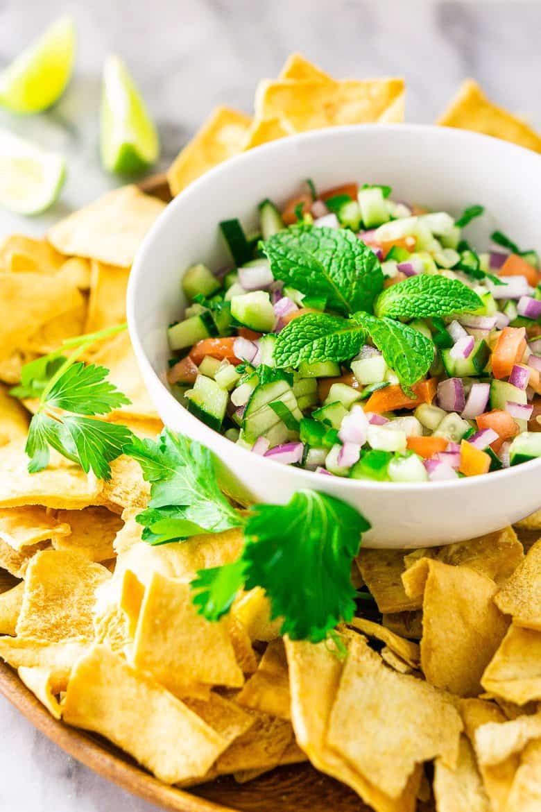 A white bowl with Mediterranean-inspired cucumber pico de gallo with pita chips and limes.