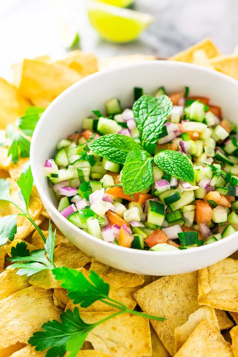 A bowl of Mediterranean cucumber salsa surrounded by pita chips and parsley.
