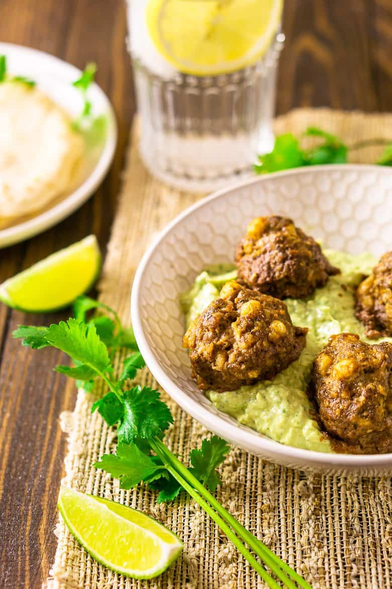 Mexican meatballs in a shallow bowl with avocado-crema sauce with cilantro and lime slices.