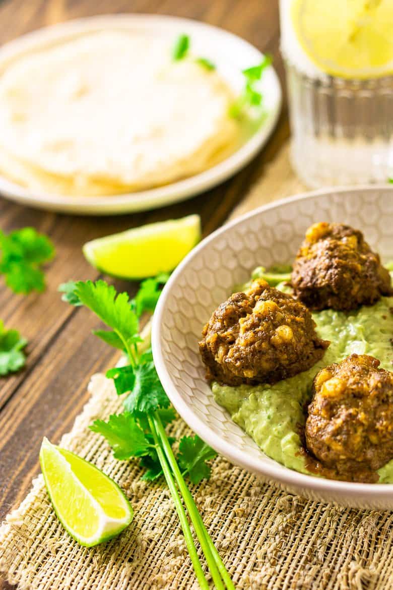 A close-up view of the Mexican meatballs on the avocado-crema sauce in a shallow bowl.