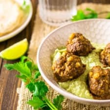 Mexican meatballs in a shallow bowl with avocado-crema sauce with cilantro and lime slices.