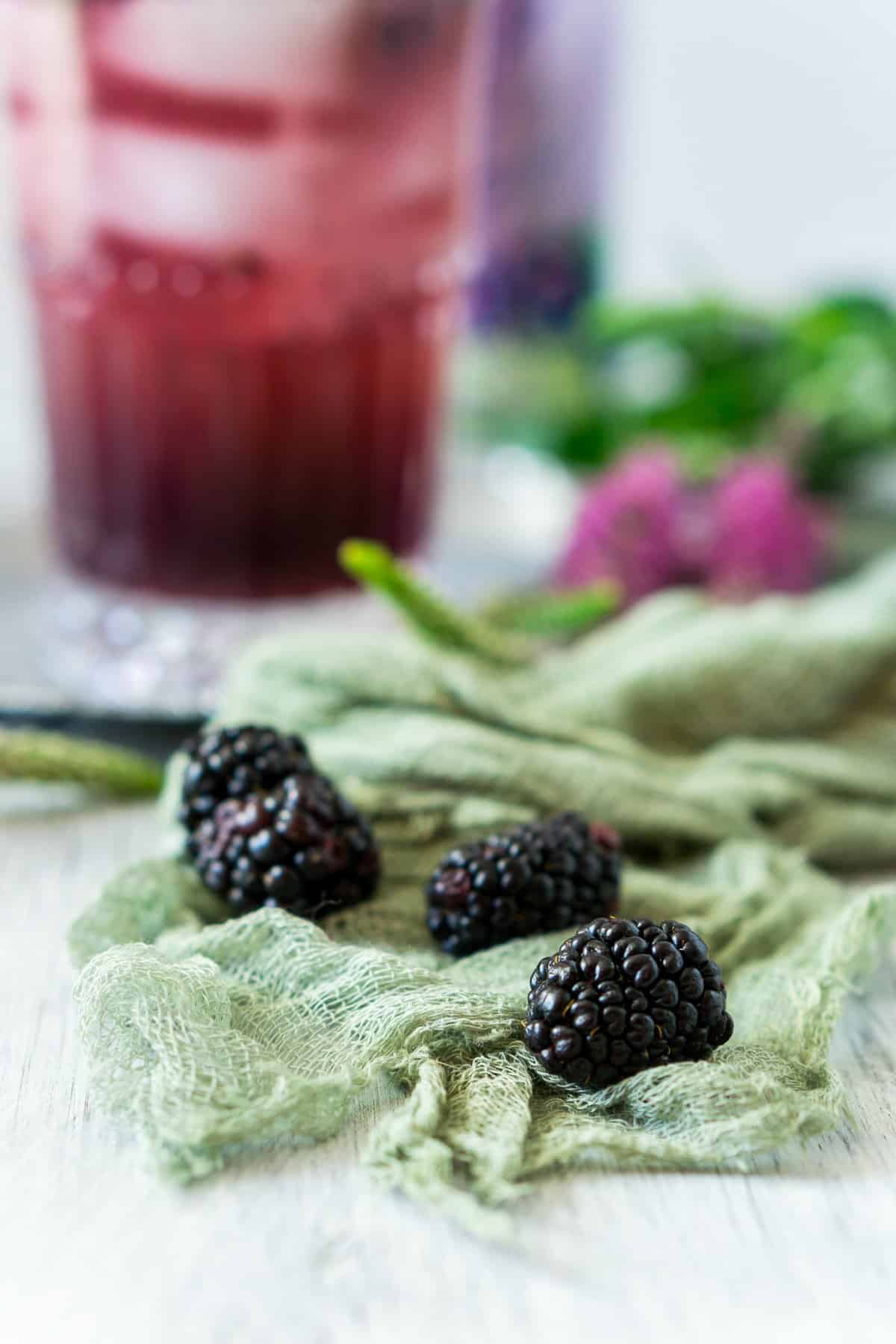 A few blackberries on green cheesecloth with purple flowers in the background.