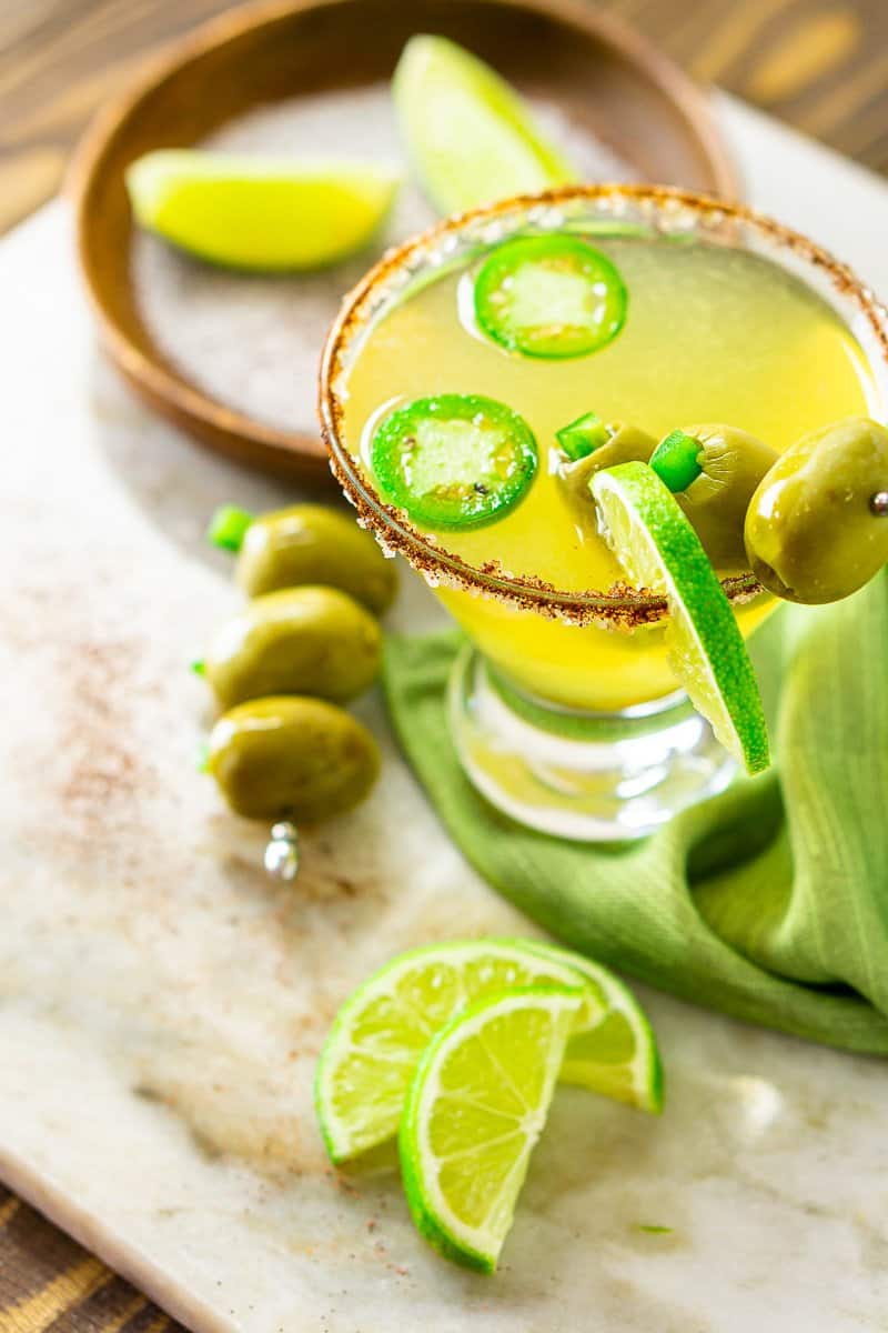 A spicy Mexican martini on a marble platter with garnishes around it.