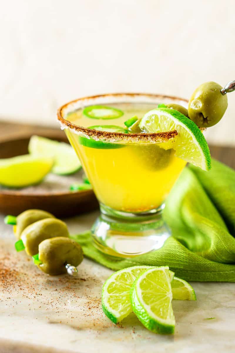 A spicy Mexican martini with lime slices and a steel toothpick with olives on it.