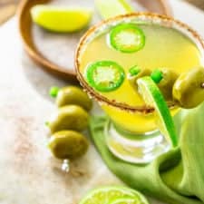 A spicy Mexican martini on a marble platter with garnishes around it.