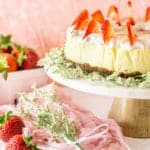 The fresh strawberry-ginger cheesecake on a marble cake platter with flowers and strawberries around it.
