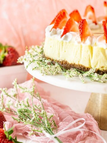 The fresh strawberry-ginger cheesecake on a marble cake platter with flowers and strawberries around it.