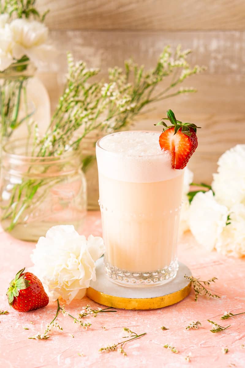 A strawberry-rhubarb gin fizz on a marble coaster with white flowers surrounding it.