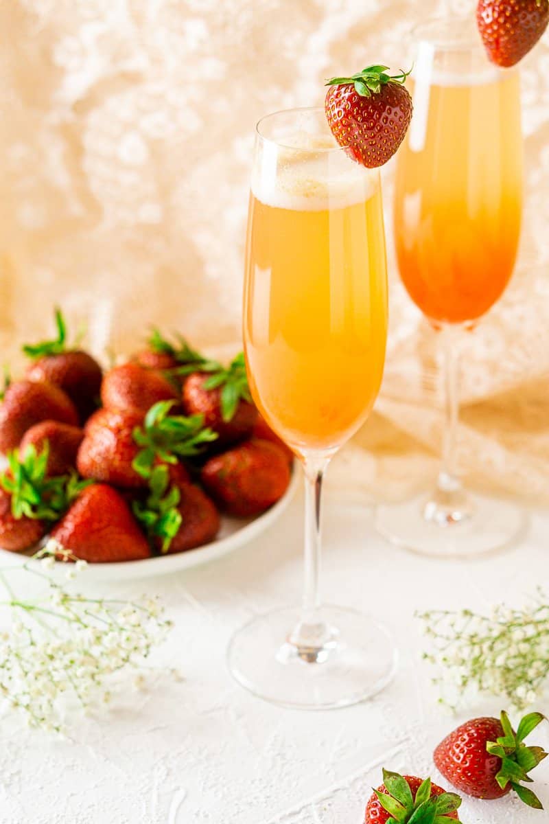 Two strawberry-rhubarb mimosas on a white background with strawberries on a white plate.
