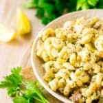 A bowl of herbed bacon macaroni salad with fresh parsley and lemon slices on the side.