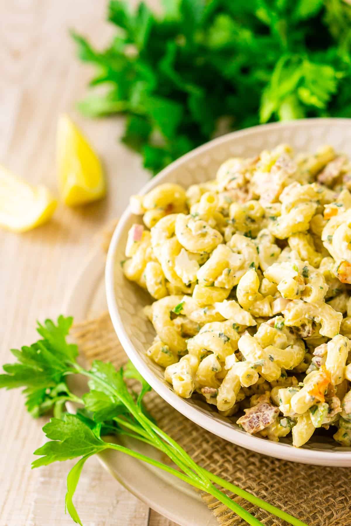 A bowl of herbed bacon macaroni salad with fresh parsley and lemon slices on the side.