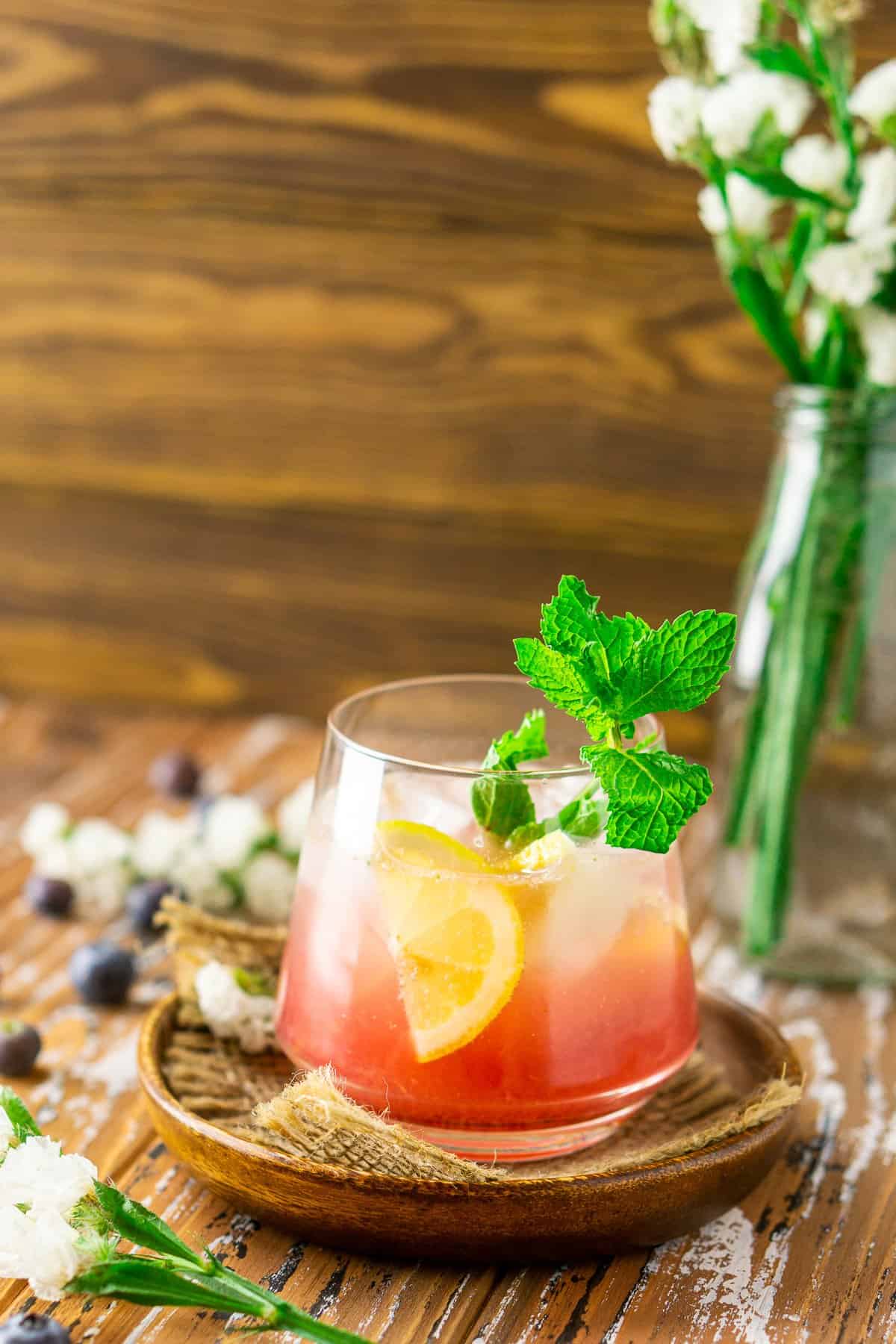 The blueberry bourbon cocktail with a flower vase on the side.