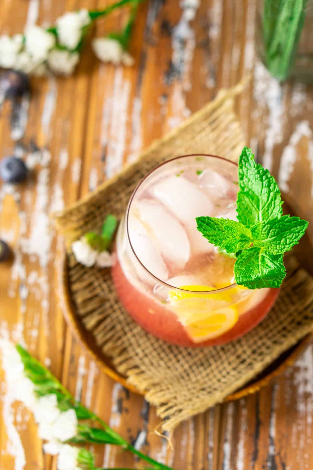 An aerial view of the blueberry bourbon smash with a sprig of mint on a wooden plate.