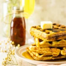 A stack of perfect buttermilk waffles with baby's breath flowers, syrup and a mimosa.
