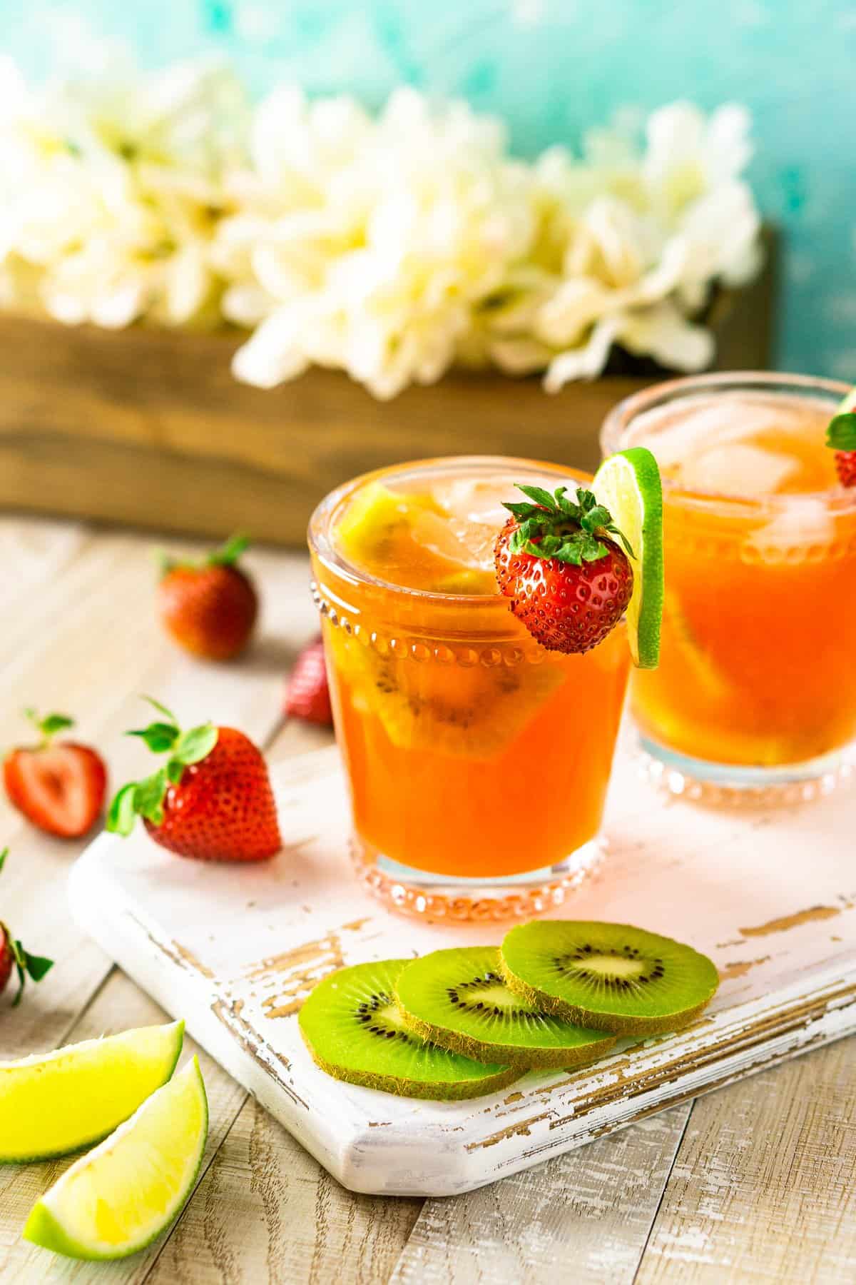 Two strawberry-kiwi margaritas on a white wooden board with white flowers.