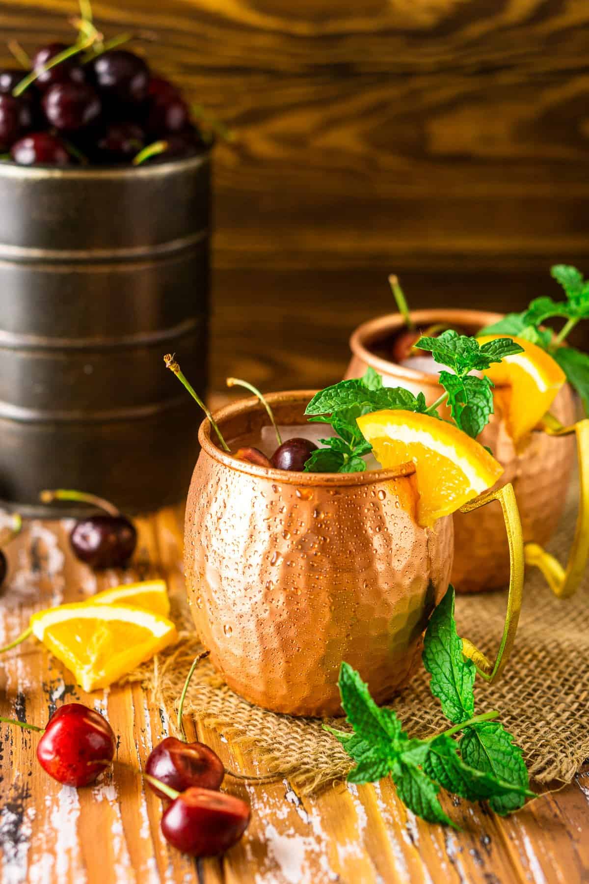 A cherry-orange Kentucky mule on burlap with cherries and orange slices around it.