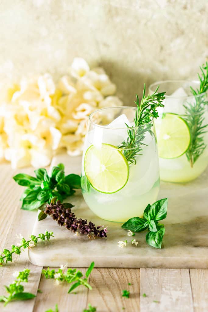 Two garden gin and tonics with basil buds in front of it.