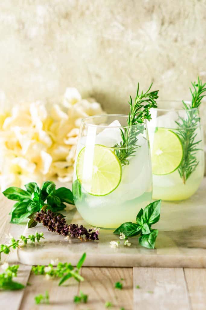 Two summer gin and tonics on a marble board with flowers and herbs on the side.