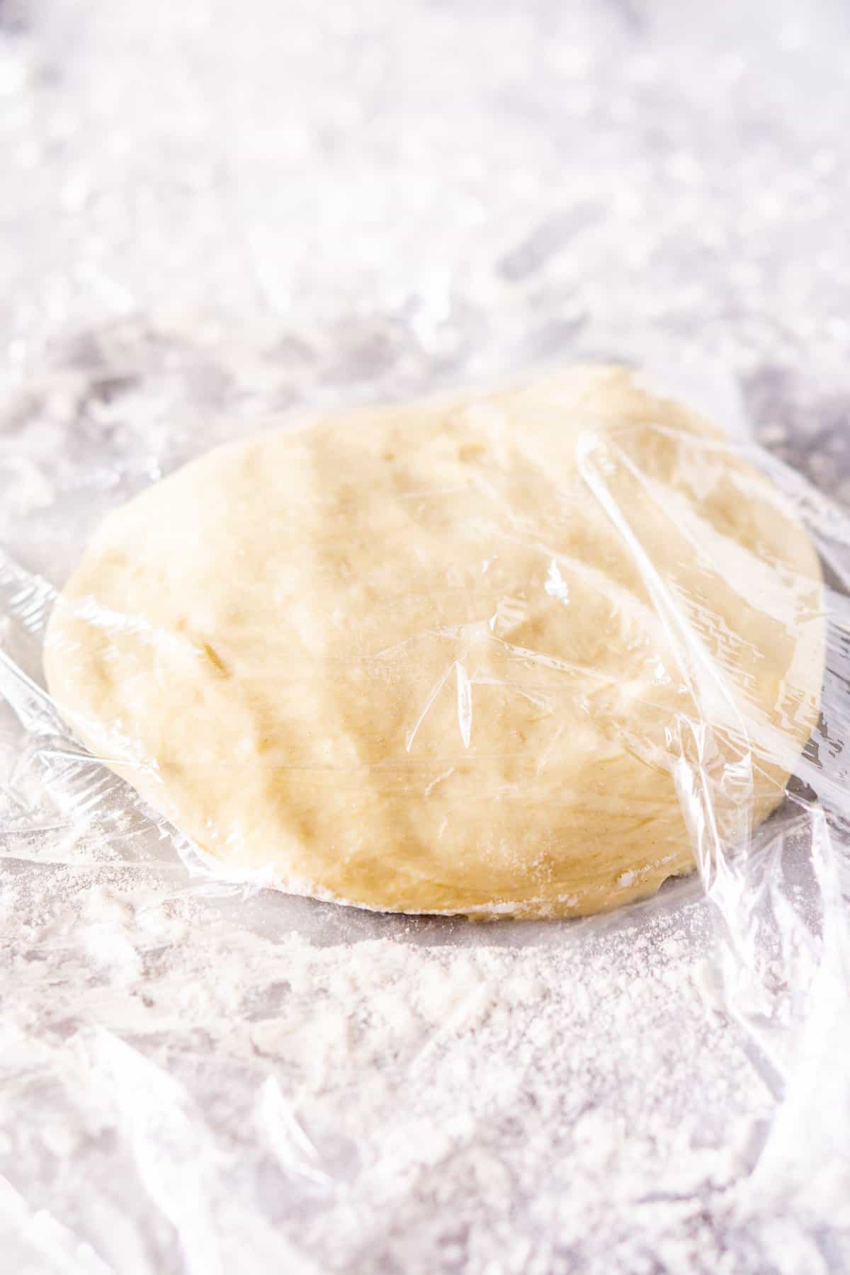 The beer pizza dough covered in plastic wrap on a floured pastry board.