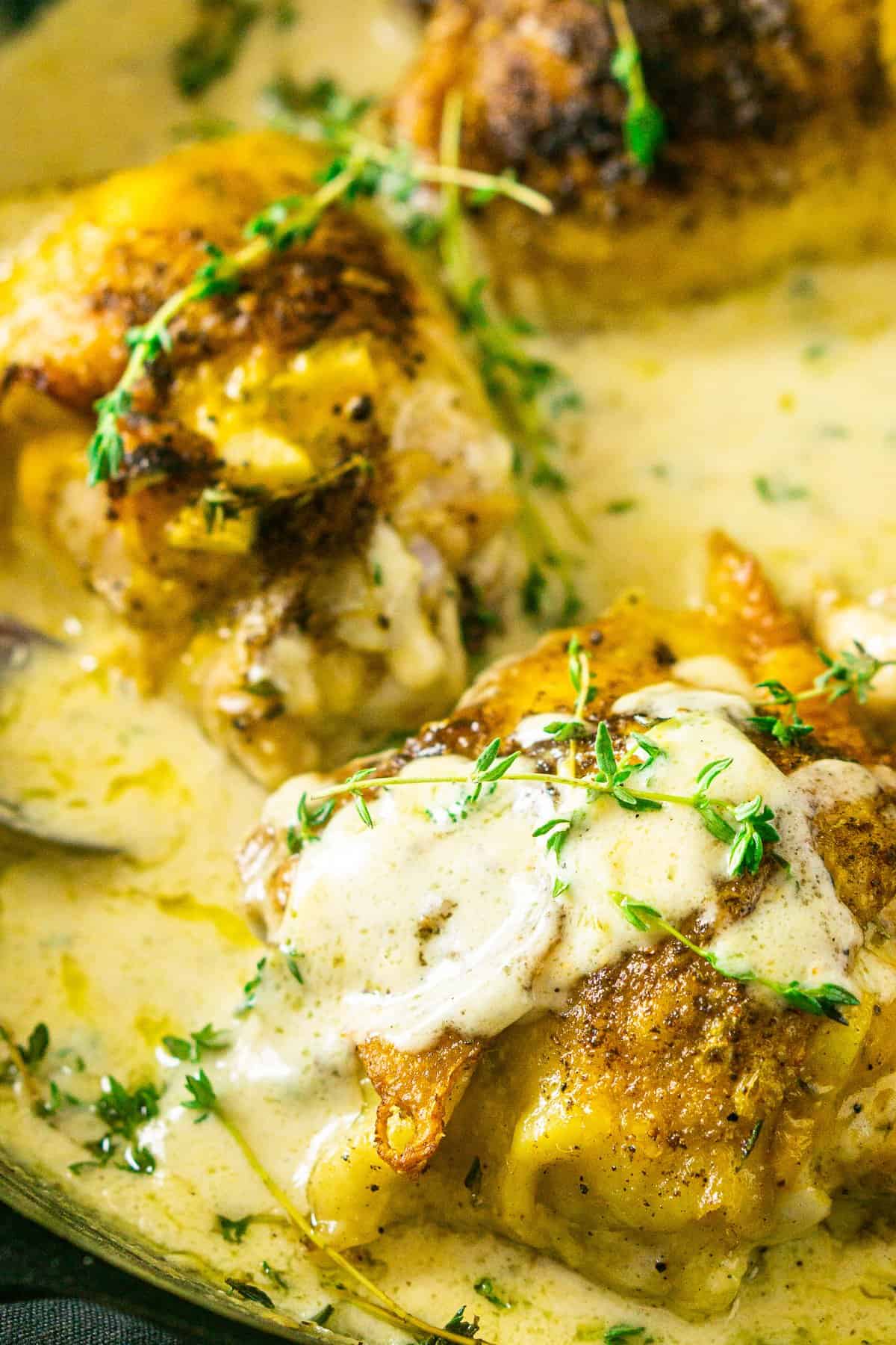 The chicken thighs in a cast-iron skillet with cream sauce spooned on top of the meat.