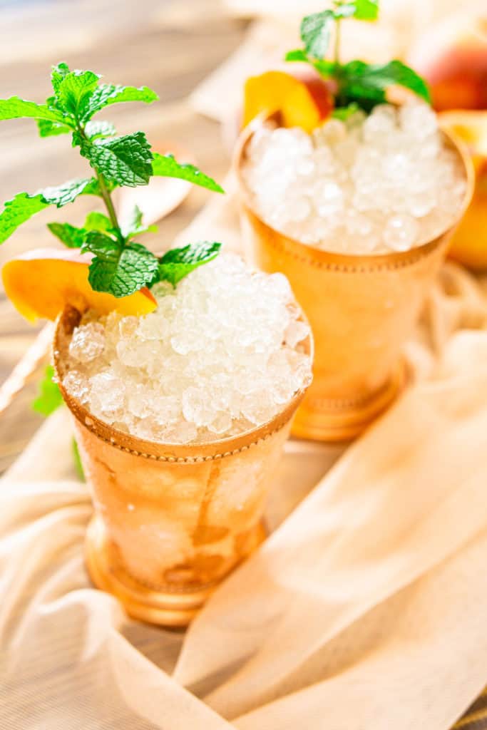 Looking down on two peach mint juleps on sheer fabric with soft lighting in the background.
