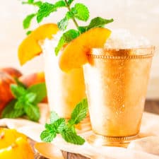 Two brown sugar-peach mint juleps with fresh mint sprigs and peach slices on the side.