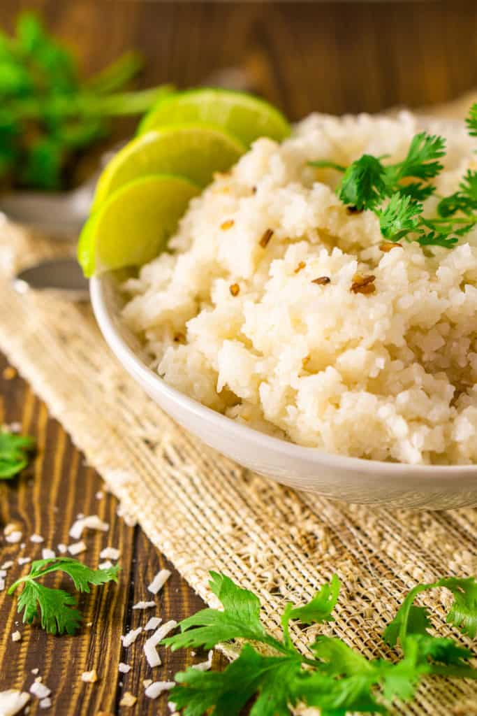 The coconut-lime rice in a white bowl on a placemat with lime slices.