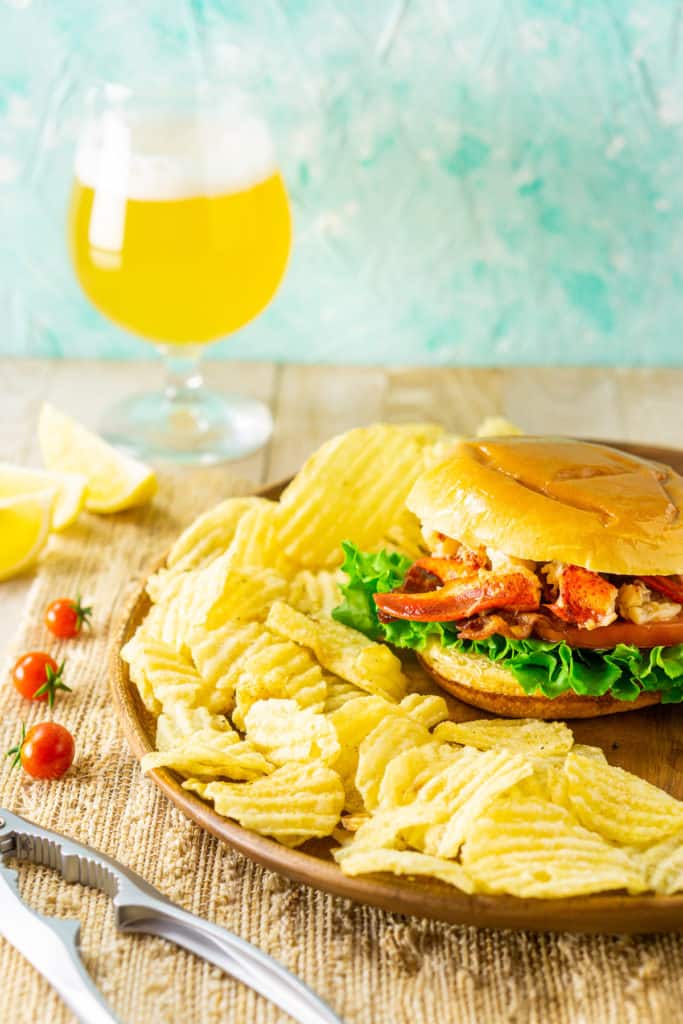 Looking down on the Connecticut-style lobster BLT on a light-colored placemat with a beer and claw cracker.