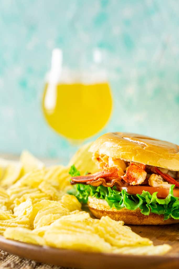 A close-up view of a Connecticut lobster BLT with chips on the side on a wooden plate.