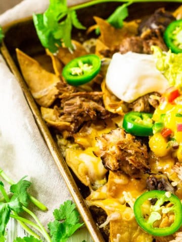 A sheet pan of jerk pork nachos with cilantro and limes on the side.