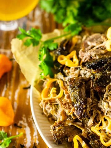 A pile of shredded Jamaican jerk pork shoulder on a plate with a beer, cilantro, and habanero peppers on the side.