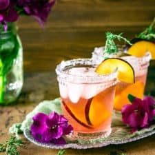 Two plum-thyme margaritas on a silver tray with a purple flower and thyme.