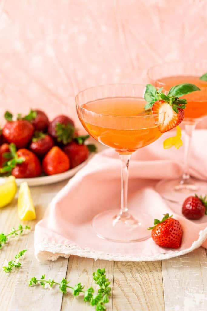 Two strawberry limoncello martinis with a plate of strawberries in the background.