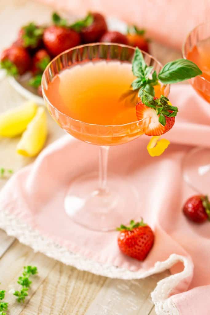 Looking from the side at a strawberry-basil limoncello martini with garnishes around it.