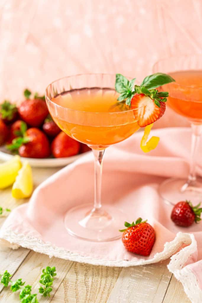 A strawberry limoncello martini with a strawberry on the side and lemon slices in the background.