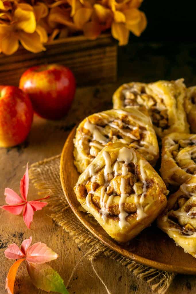 Looking down on a plate of apple cinnamon rolls with apples and leaves to the side.