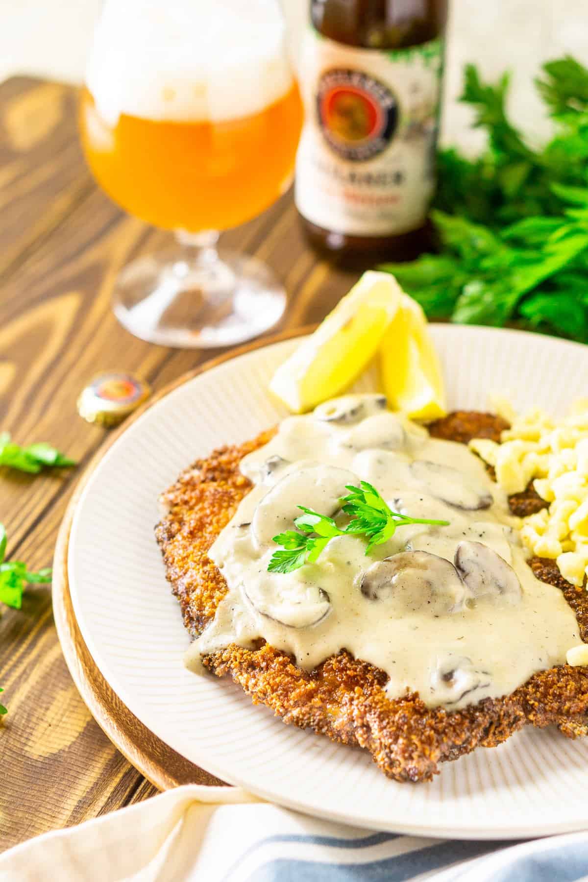 A side shot of the beer-brined schnitzel with mushroom gravy and a beer in the background.